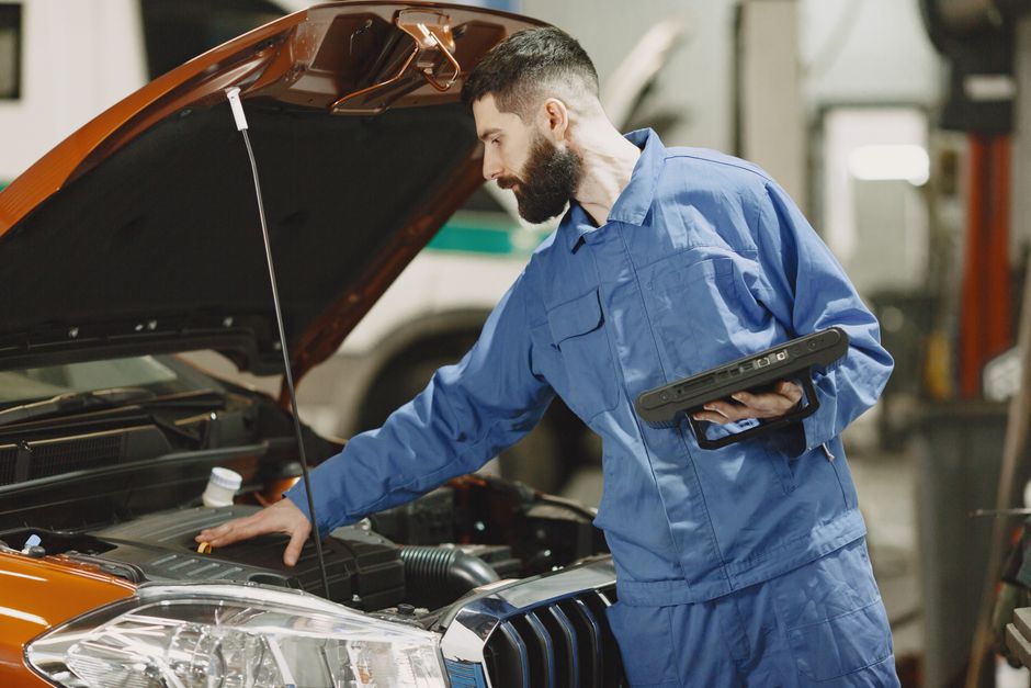 Professional mechanic examining a car engine under an open hood in a garage setting.